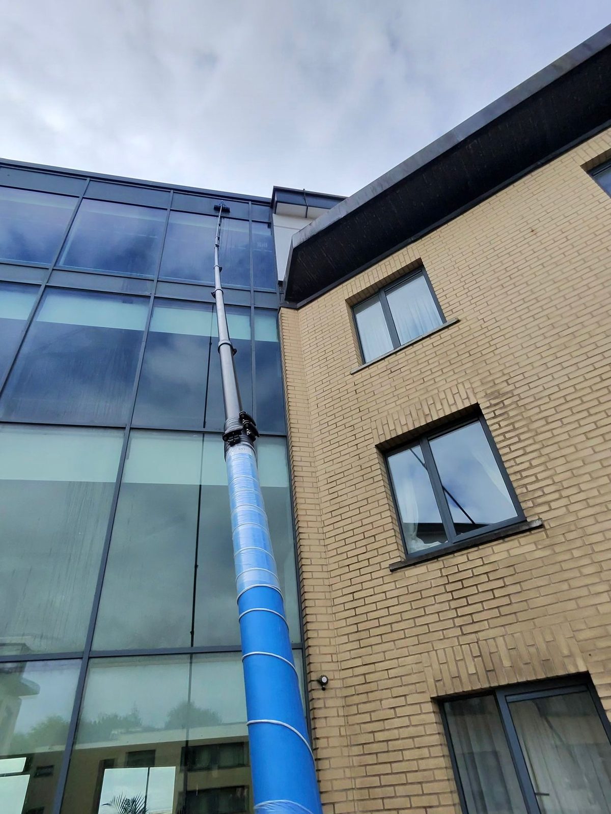 Carbon-fibre water-fed pole reaching up a multi-storey glass facade